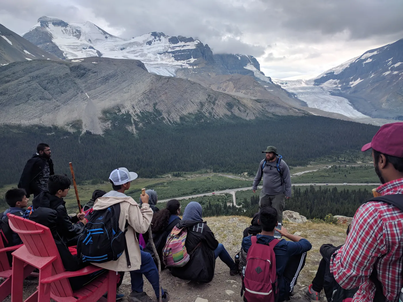 Teaching a seated group on a mountain overlook in the Canadian Rockies, a glacier and snowfield behind him.